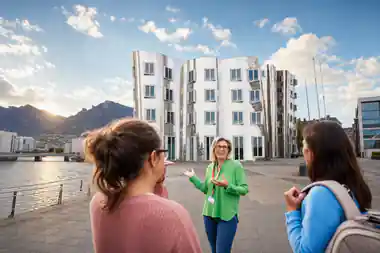 Woman in green jacket gesturing to group in courtyard