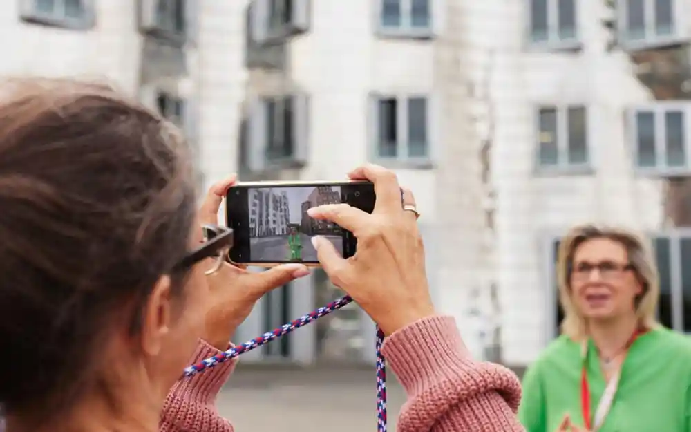 Woman photographing with phone, guide in green nearby